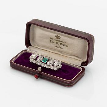 A platinum brooch set with a step-cut emerald and old- and eight-cut diamonds.