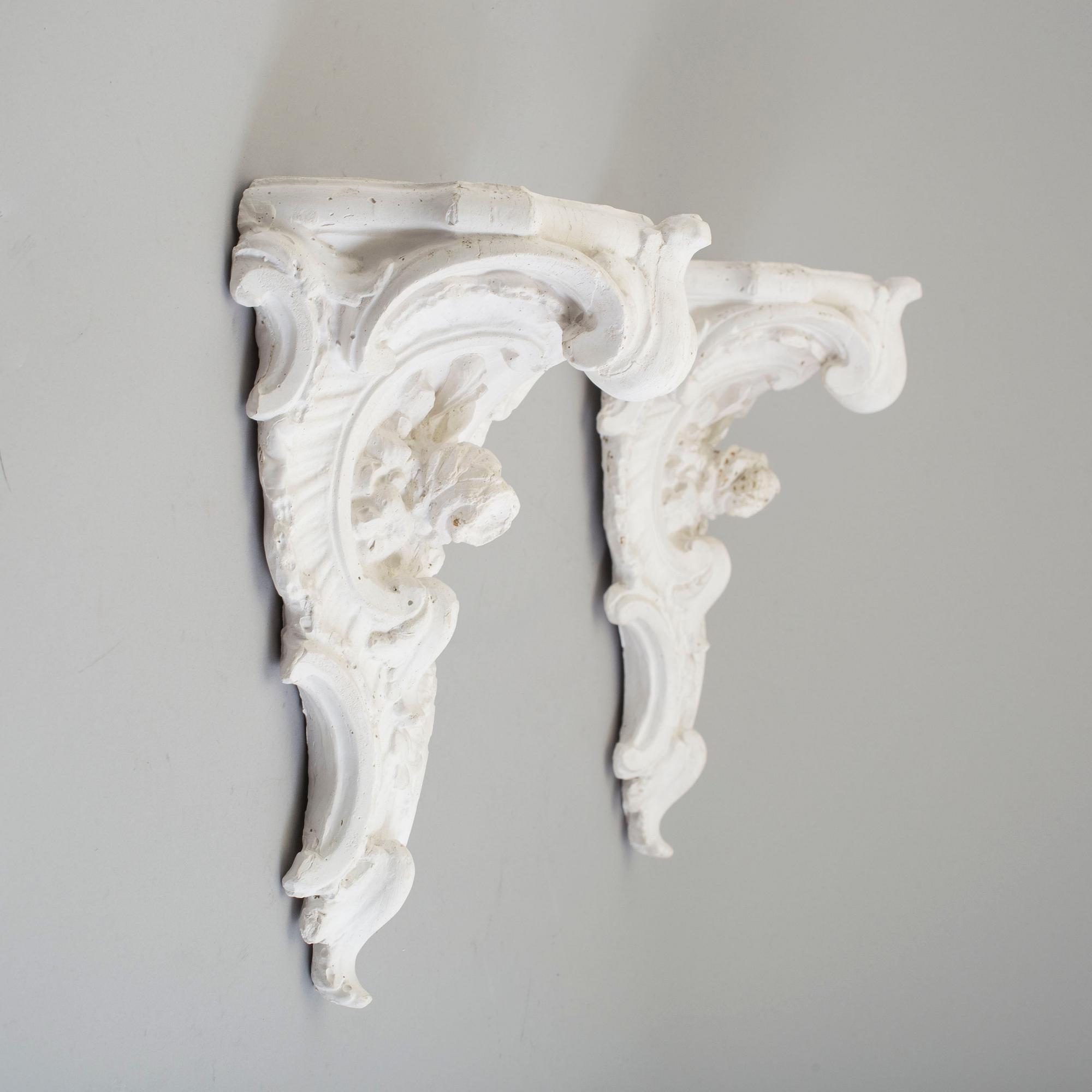 A pair of consoles and a set of three decor-elements, plaster, 20th century.