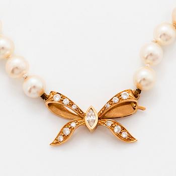 A cultured pearl necklace with a bow clasp in 18K gold set with round brilliant-cut diamonds.