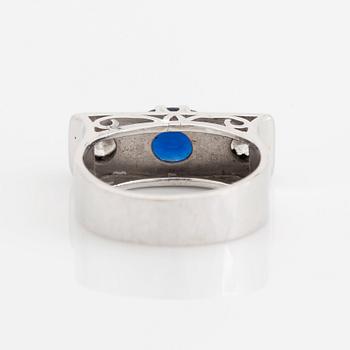 An 18K white gold ring set with a faceted sapphire, possibly synthetic, and round brilliant-cut diamonds.