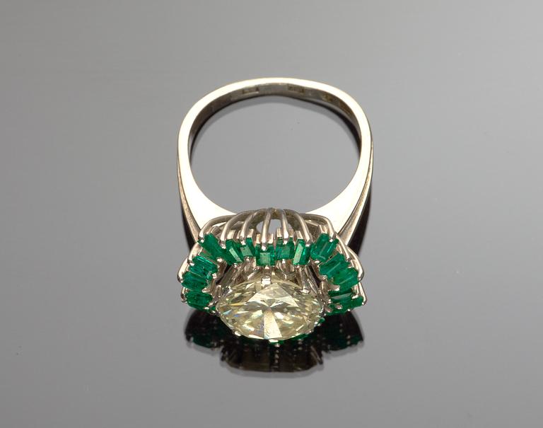 RING, briljantslipad diamant, tot. ca 4.60 ct med krans av bagetteslipade smaragder. 1970-tal.