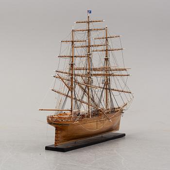 A wooden scale model of Cutty Sark on a painted wooden stand.