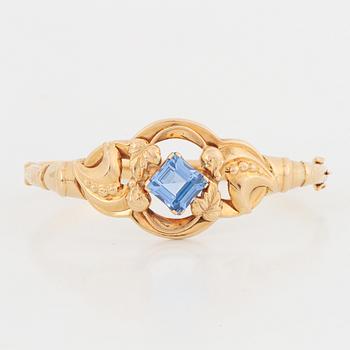 An 18K gold bangle set with a blue synthetic stone.