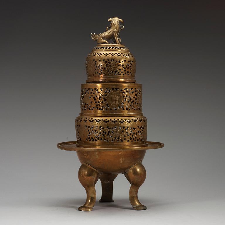 A four-part brass tripod censer, pierced sections with lotus scrolls and a fo-dog finial, late Qing dynasty (1644-1912).