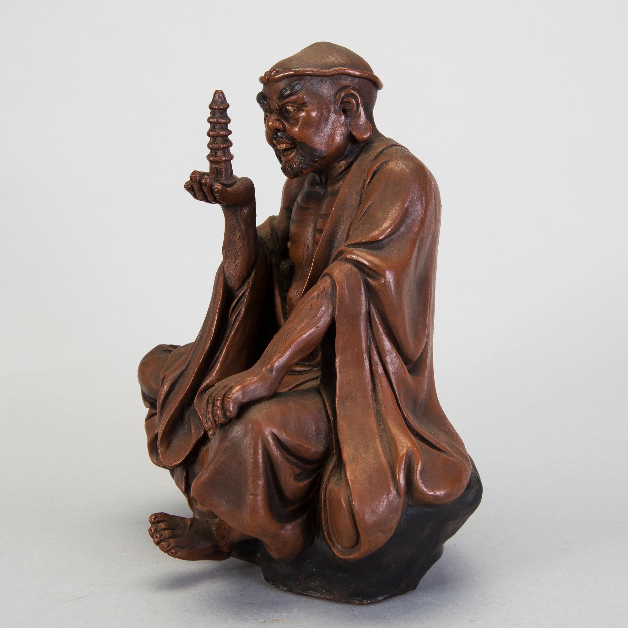 A Japanese earthenware seated figure of a man holding a pagoda, 20th century.