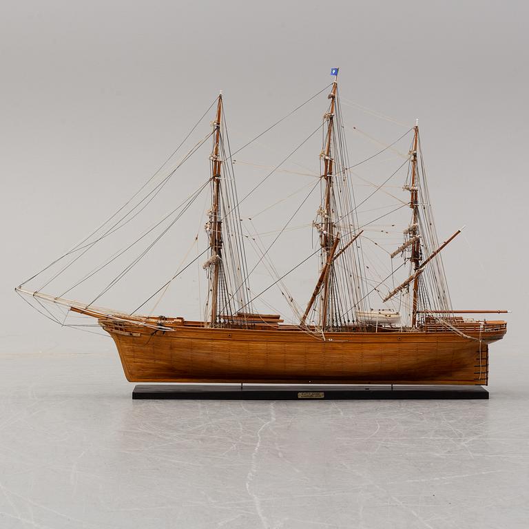 A wooden scale model of Cutty Sark on a painted wooden stand.