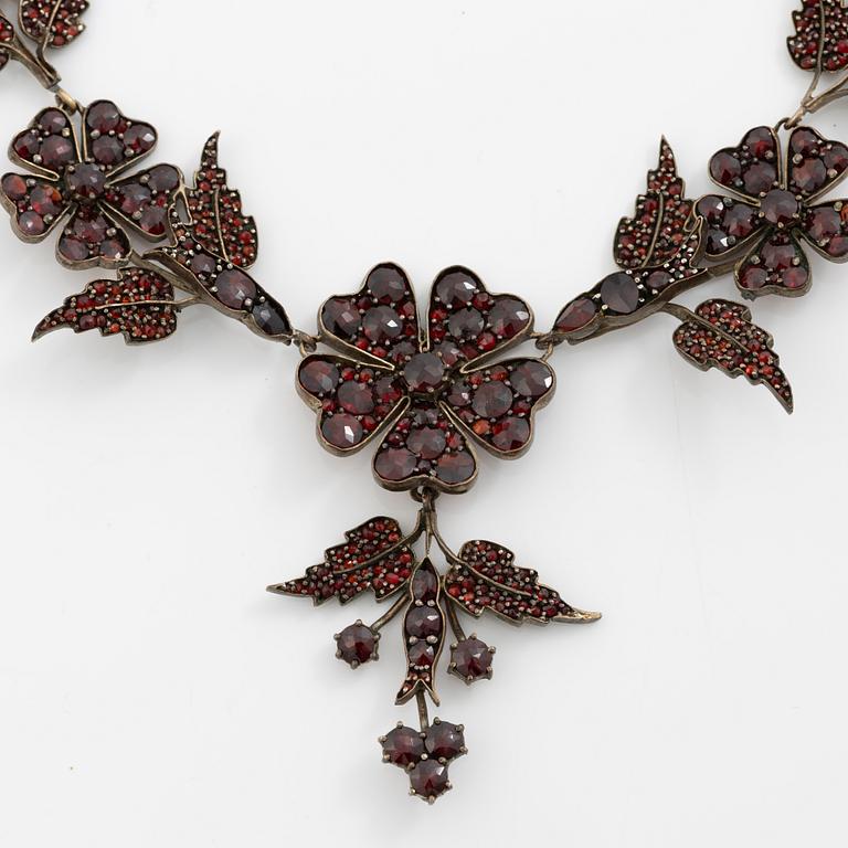 Garniture, necklace/bracelet and earrings in silver with garnets in the form of floral motifs, around the turn of the 20th century.