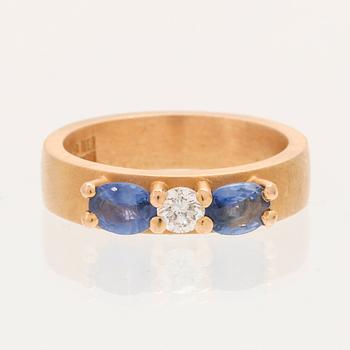 A ring containing at least 21.6K gold, set with a round cut brilliant diamond and oval brilliant cut sapphires.