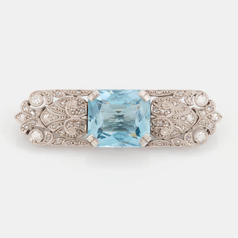 An 18K white gold brooch set with a faceted aquamarine and round brilliant- and rose-cut diamonds.