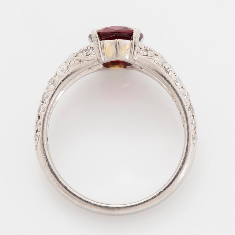 A platinum ring set with a faceted ruby and round brilliant-cut diamonds.