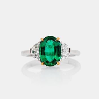 A 2.29ct oval-cut emerald ring. The emerald flanked by half moon shaped diamonds, total carat weight circa 0.81ct.