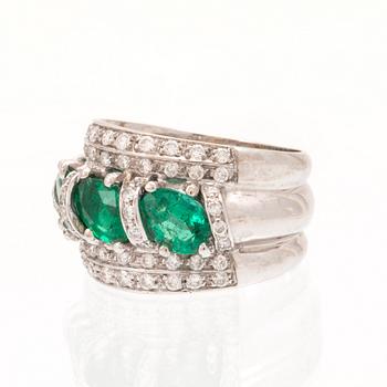 An 18K white gold ring set with oval cut emeralds and round brilliant cut diamonds.