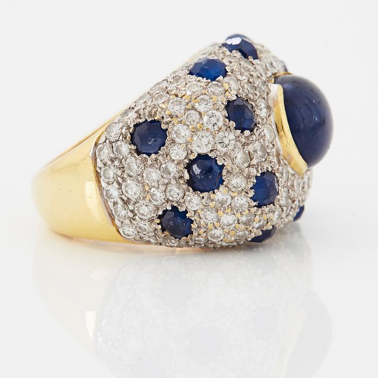 An 18K gold ring set with a cabochon-cut sapphire and round brilliant-cut diamonds and faceted sapphires.