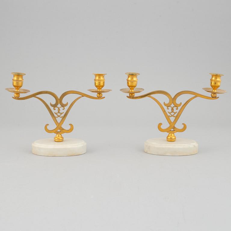 A pair of brass candle sticks om marble stands from the middle of 20th century.