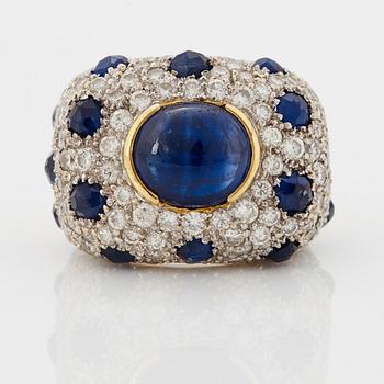 An 18K gold ring set with a cabochon-cut sapphire and round brilliant-cut diamonds and faceted sapphires.