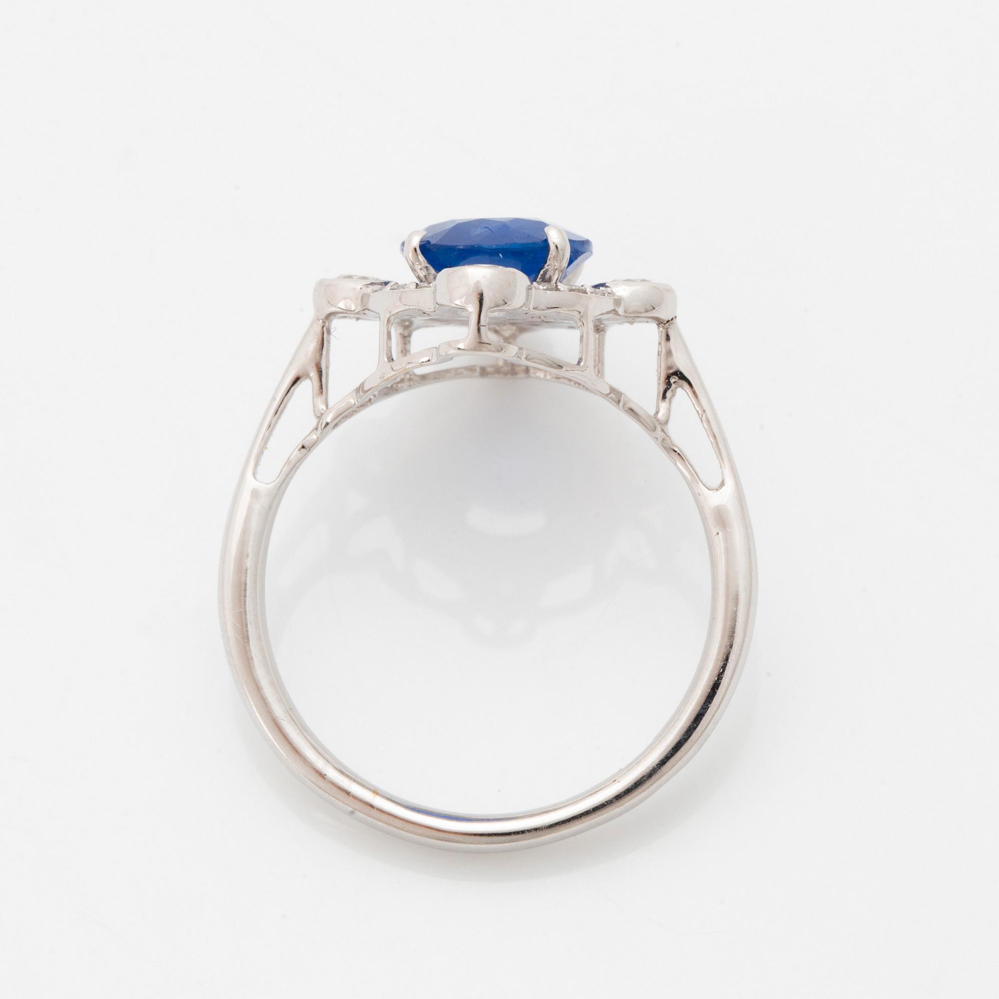 An 18K white gold ring set with a faceted sapphire and round brilliant-cut diamonds.