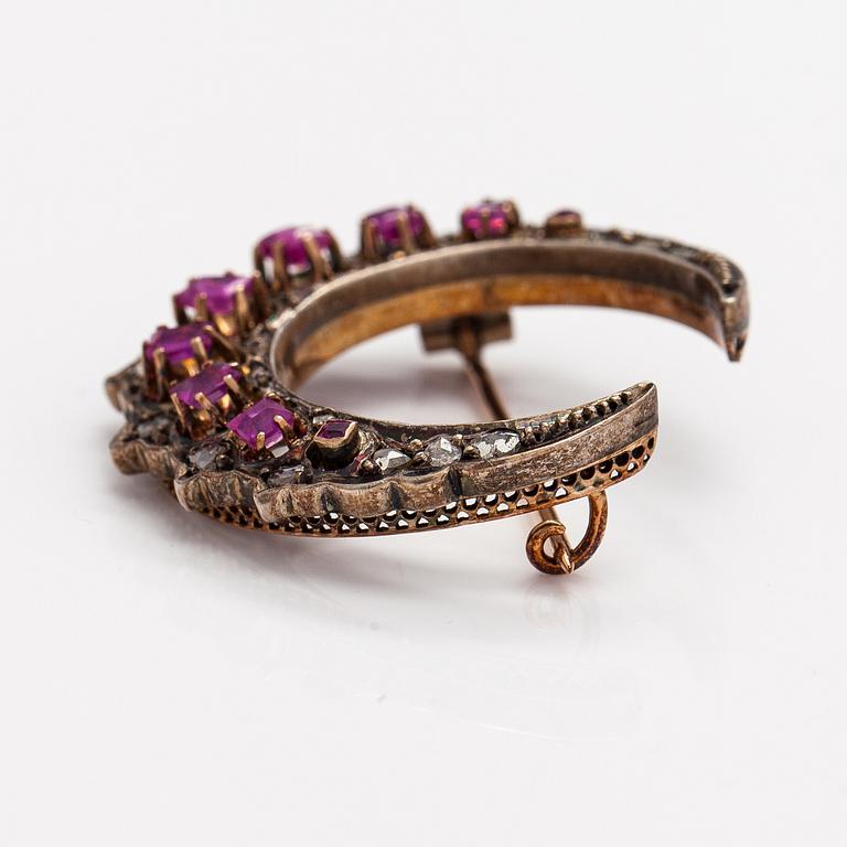 A cresent moon brooch made of 14K gold, silver, rubies and diamonds.