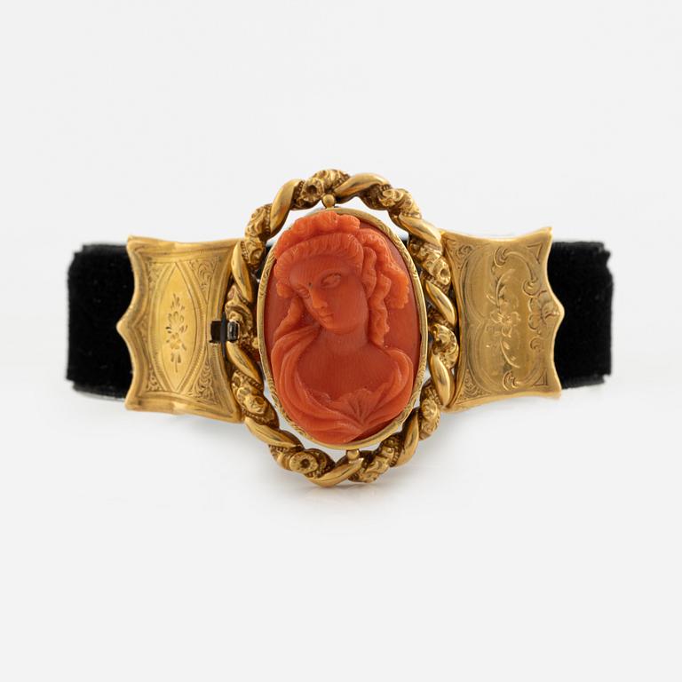 An 18K gold and coral cameo braclet with a black band.