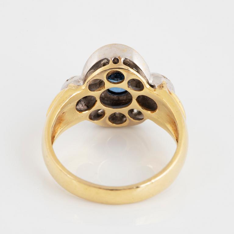 An 18K gold ring set with a synthetic sapphire and round brilliant-cut diamonds.