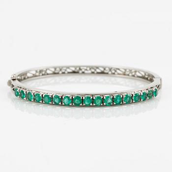 A bangle of low carat gold with faceted emeralds.