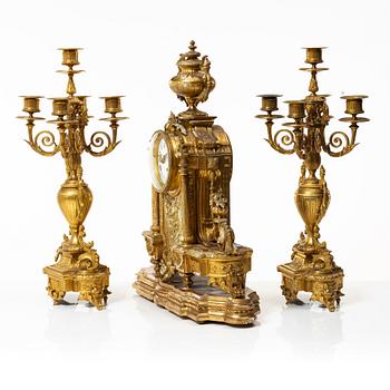 A mantle clock and a pair of candelabra, Louis XVI style, ca 1900.