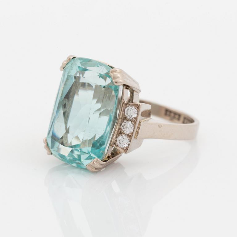 An 18K white gold ring set with a faceted aquamarine and round brilliant-cut diamonds.