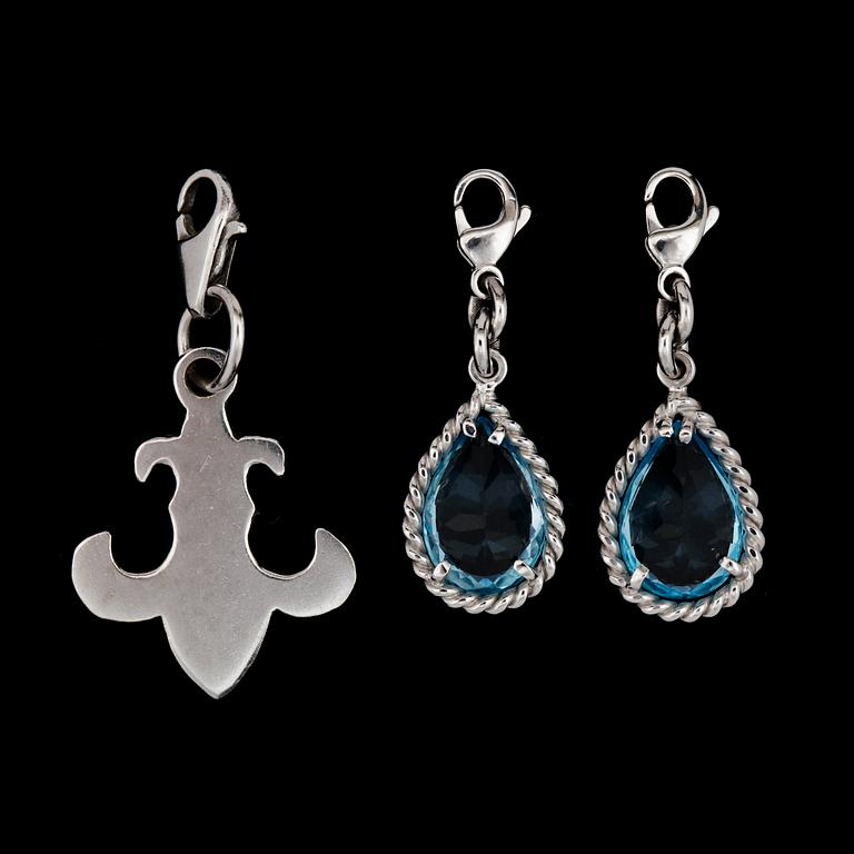 Two white gold and blue topas charms.