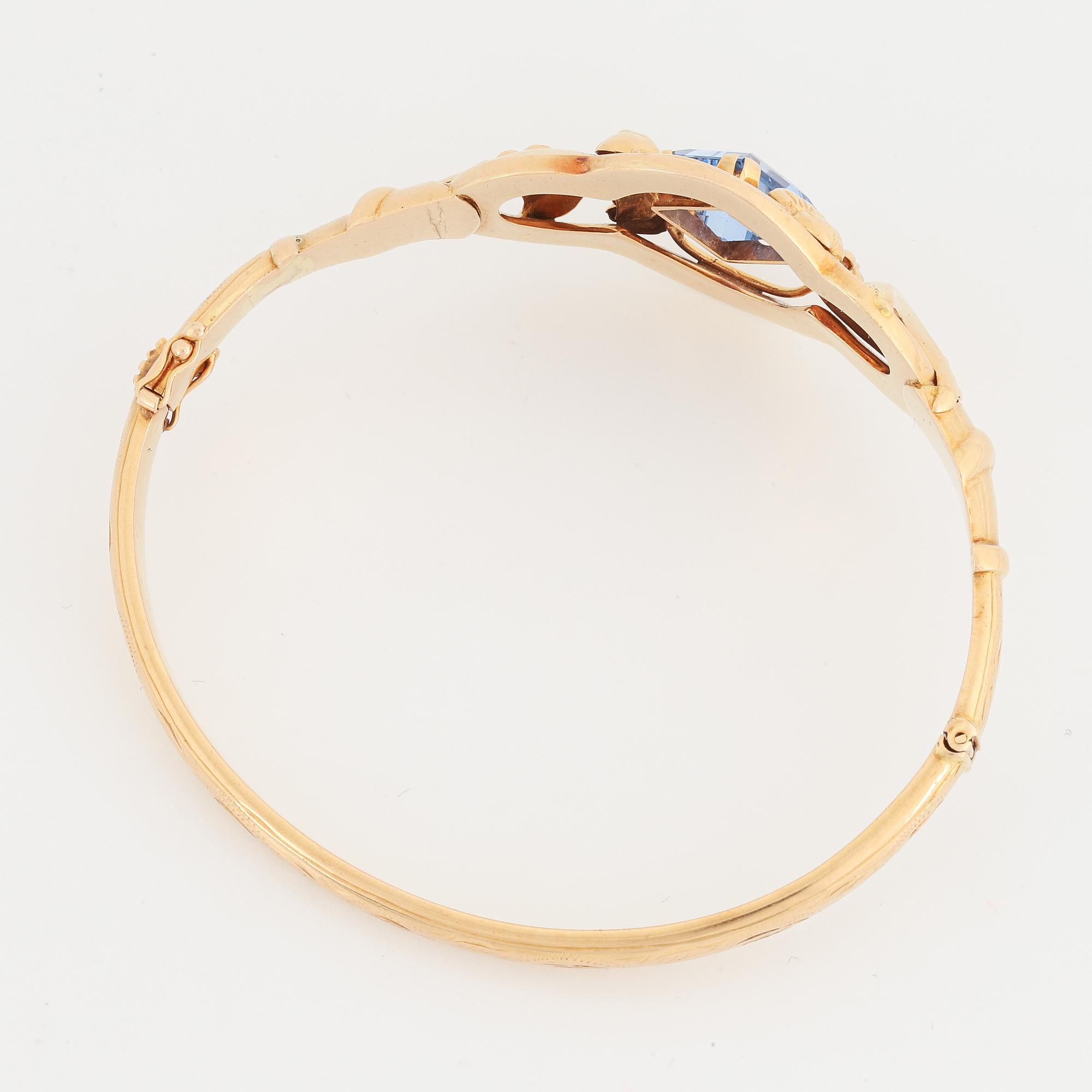 An 18K gold bangle set with a blue synthetic stone.