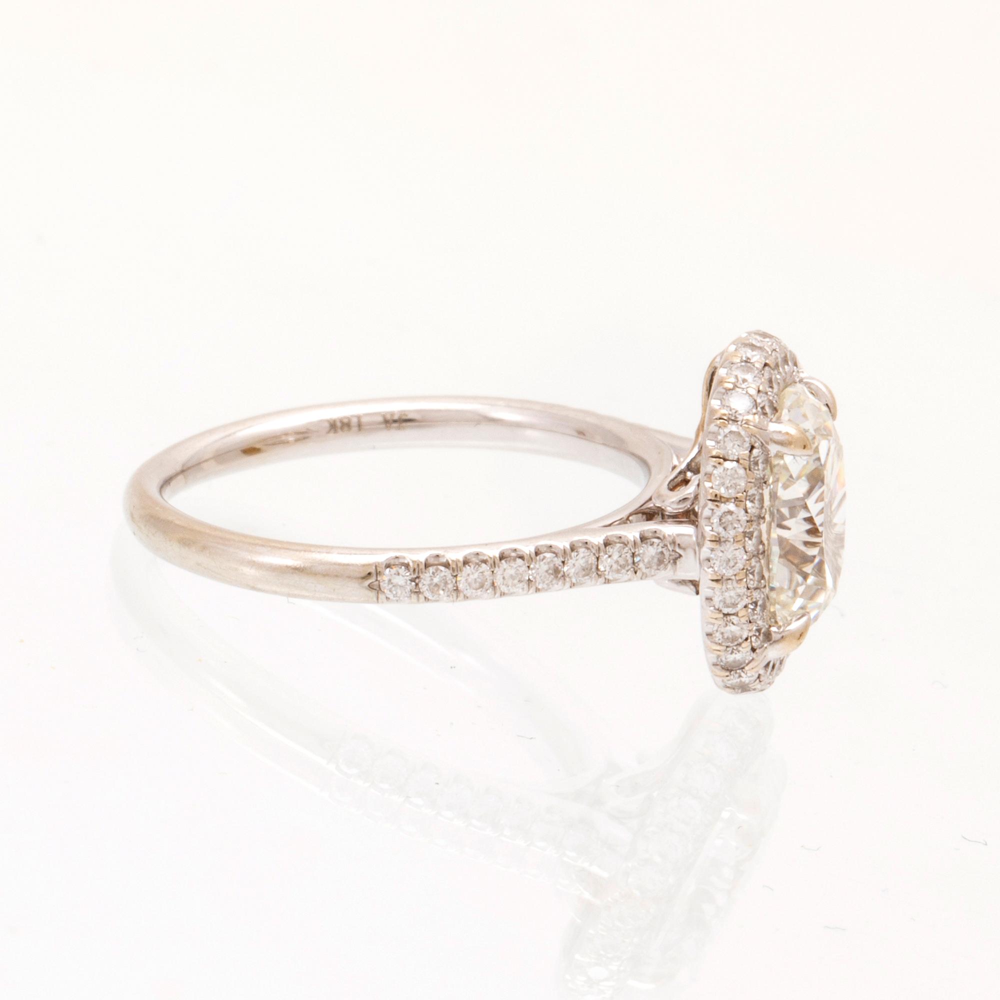 An 18K white gold ring by James Allen, set with an oval brilliant cut diamond in a halo of round brilliant cut diamonds.