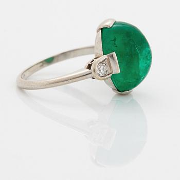 A platinum ring set with a cabochon-cut emerald and round brilliant-cut diamonds.