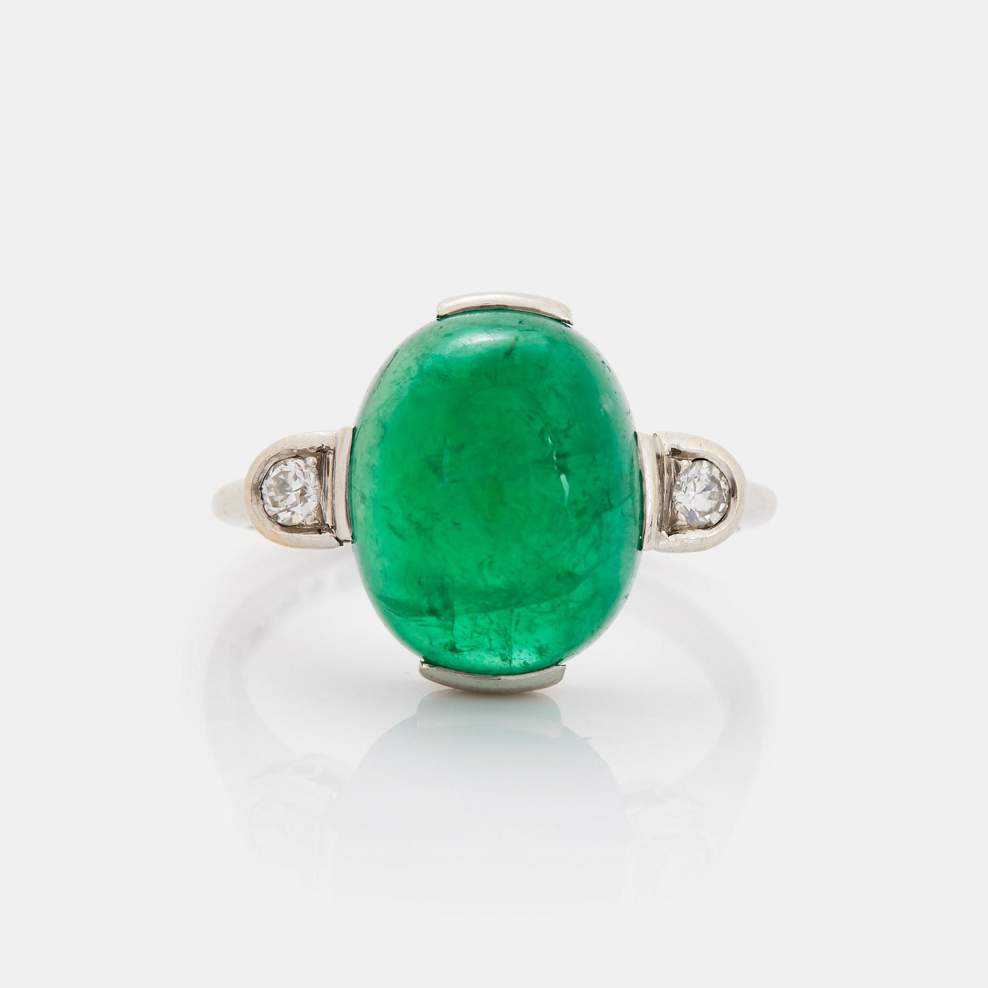 A platinum ring set with a cabochon-cut emerald and round brilliant-cut diamonds.