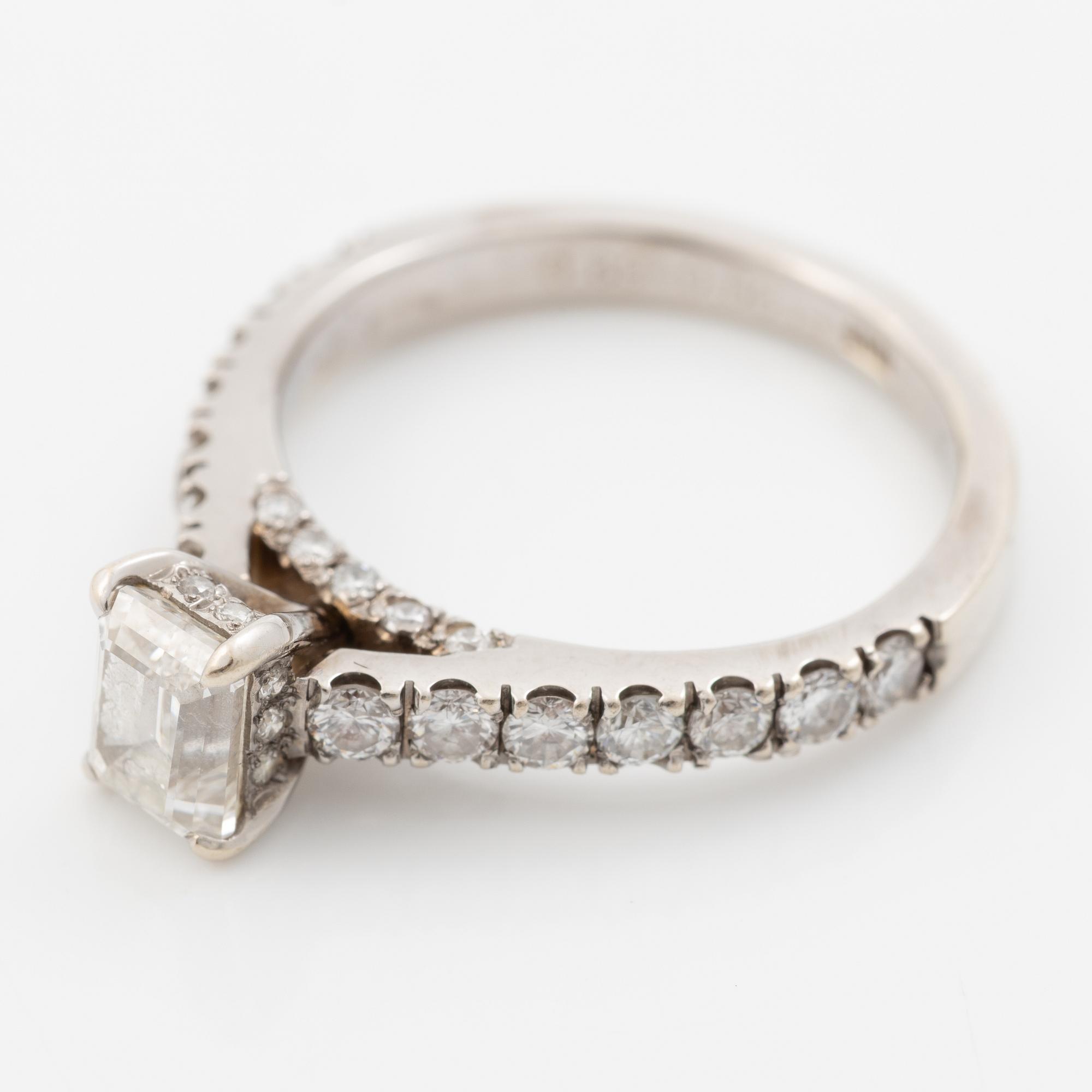 18K white gold ring set with an emerald-cut diamond and round brilliant-cut diamonds.