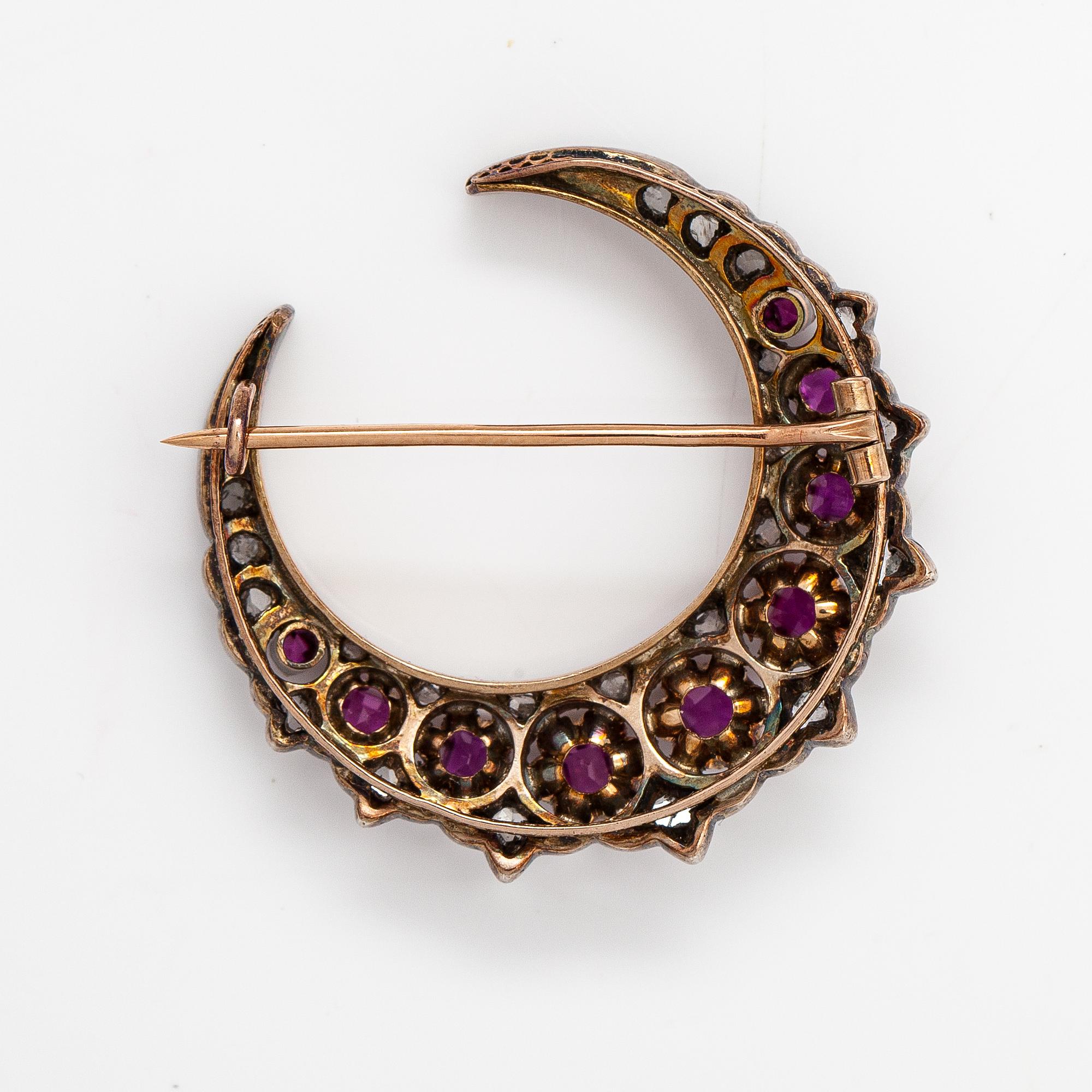 A cresent moon brooch made of 14K gold, silver, rubies and diamonds.