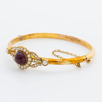 BANGLE, 10K gold, 1 cabochon garnet and seed pearls. 1900s. Hinged mechanism.