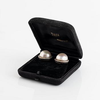 A pair of 18K white gold earrings set with cultured mabe pearls and round brilliant-cut diamonds.