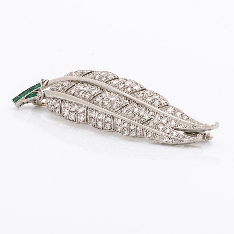 A platinum brooch set with round brilliant-cut diamonds and emeralds.