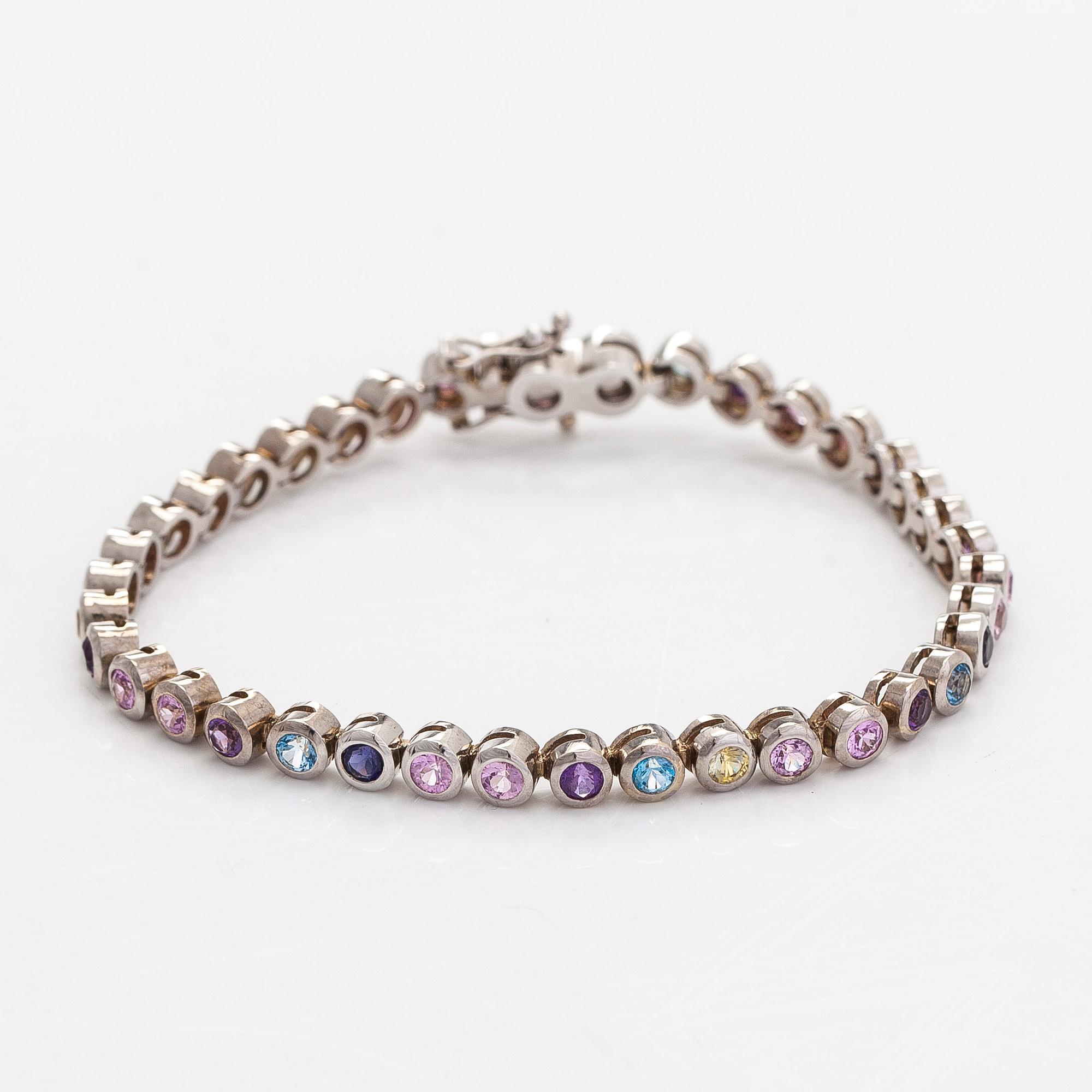 Rannekoru, 18K valkokultaa ja monivärisiä kiviä.