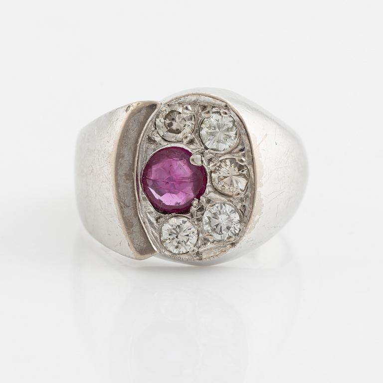 An 18K white gold ring set with a faceted ruby and round brilliant-cut diamonds.