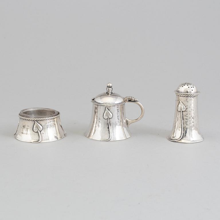 An Art Nouveau set of a silver salt cellar, pepper shaker and mustard pot, Birmingham, 1907-08 and satchel, 1906.