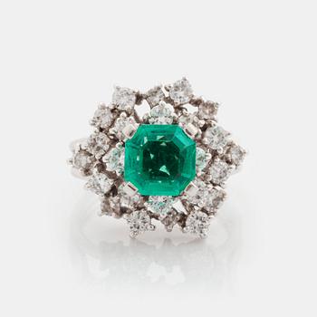 A platinum ring set with a faceted emerald and round brilliant-cut diamonds.