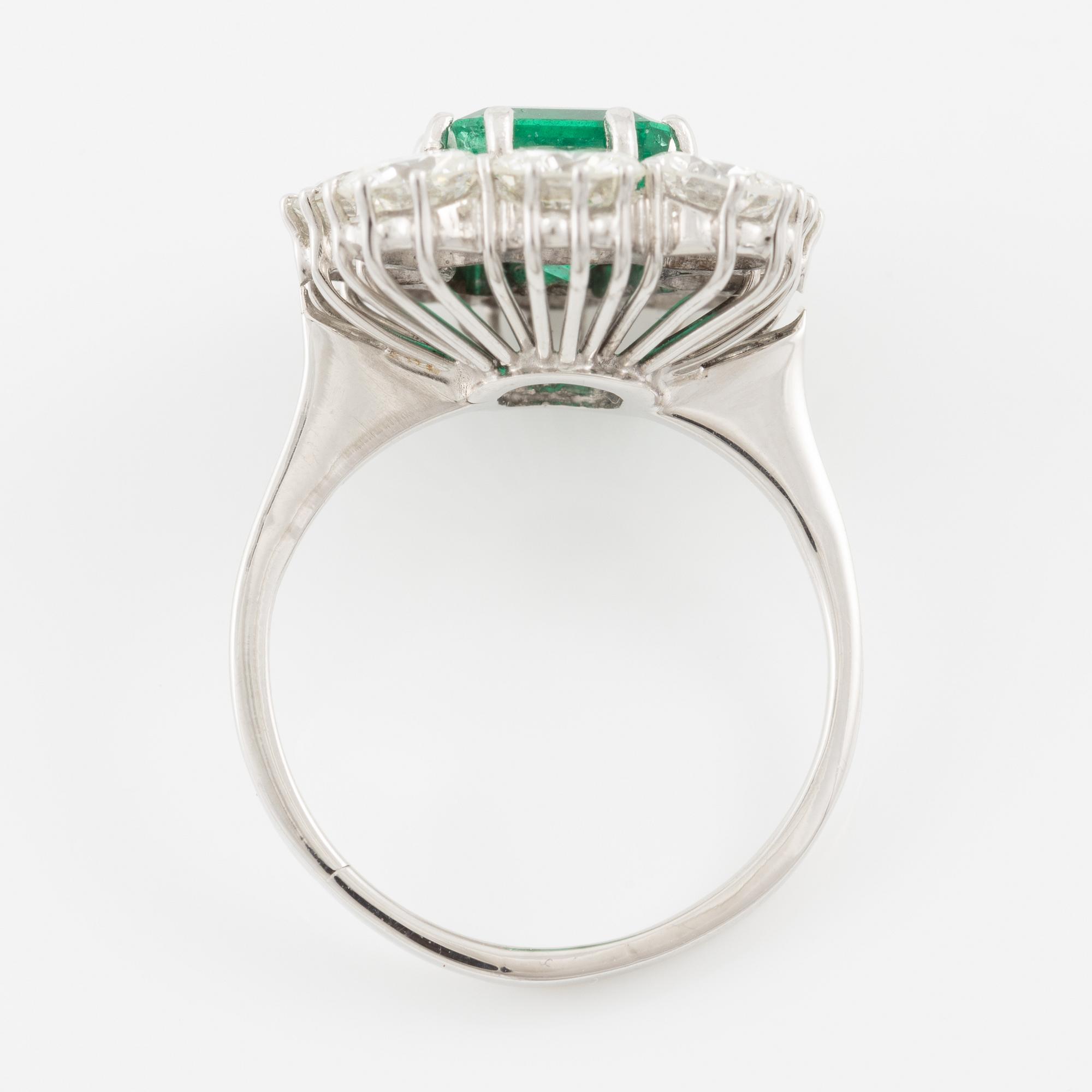 An 18K whitegold ring set with a step-cut emerald and round brilliant-cut diamonds.