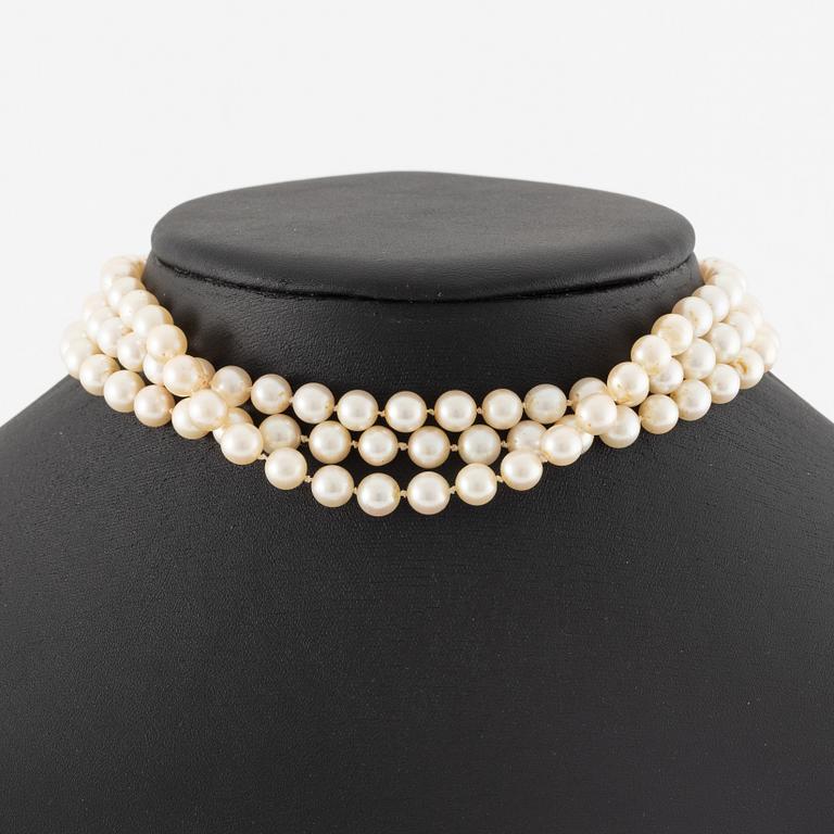 A three strand cultured pearl necklace, clasp in 18K gold with white stones and emeralds.