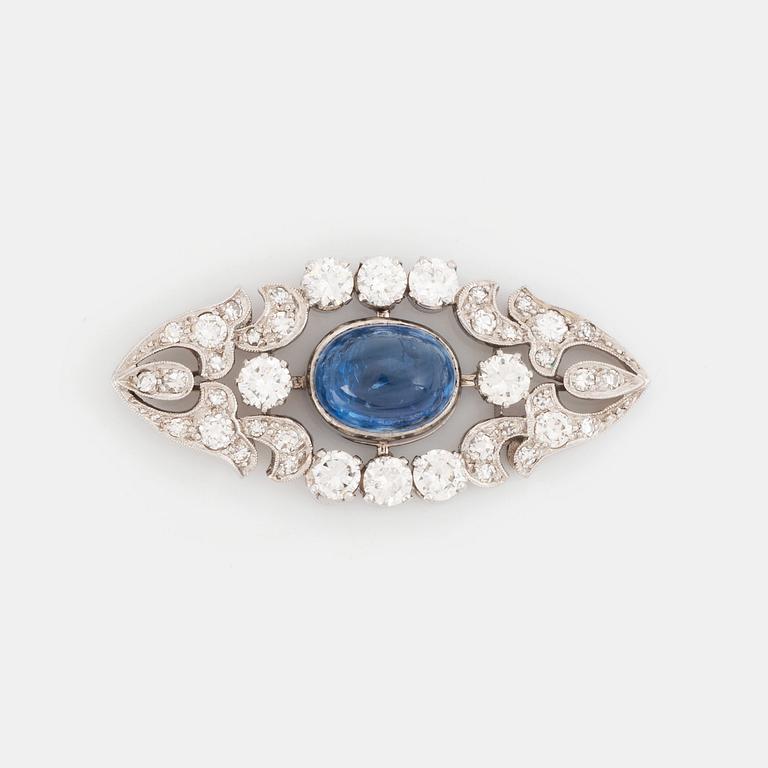 A platinum brooch set with a cabochon-cut sapphire and a cabochon-cut emerald.