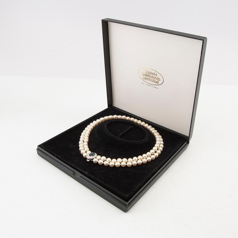 Necklace of cultured pearls with an 18K white gold clasp featuring an oval faceted sapphire and round brilliant-cut diamonds.