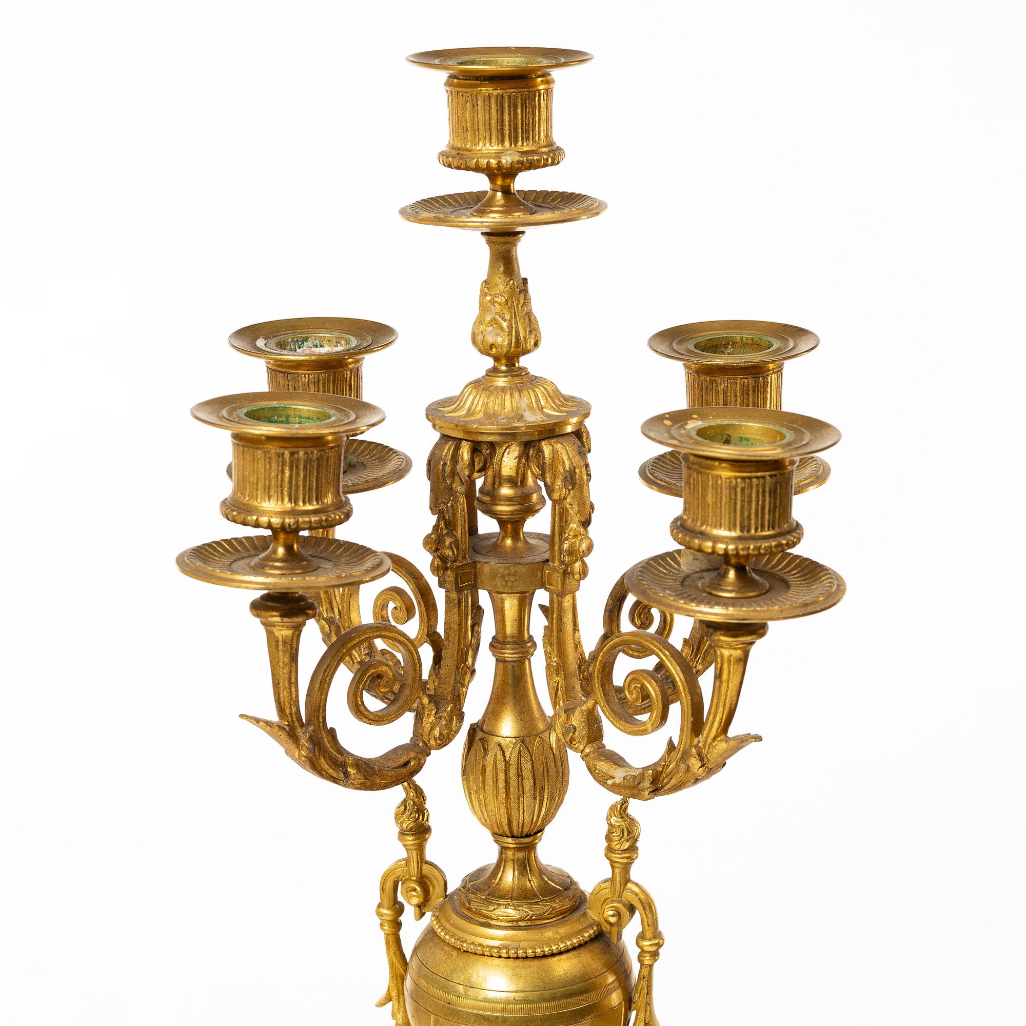 A mantle clock and a pair of candelabra, Louis XVI style, ca 1900.