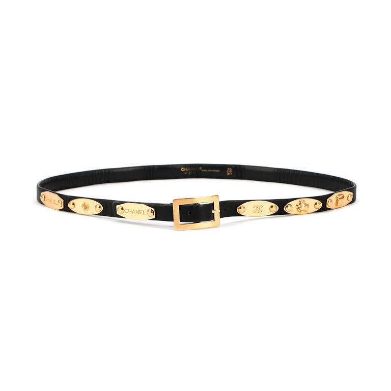 CHANEL, a skinny black leather belt with gold colored hardwear.