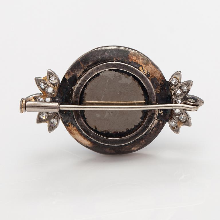 An palladium, silver and gold brooch with a metal pin, enamel decor and diamonds ca. 1.38 ct in total.