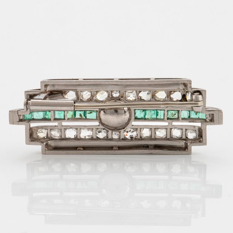 A platinum brooch set with old- and rose-cut diamonds, faceted emeralds and a pearl.