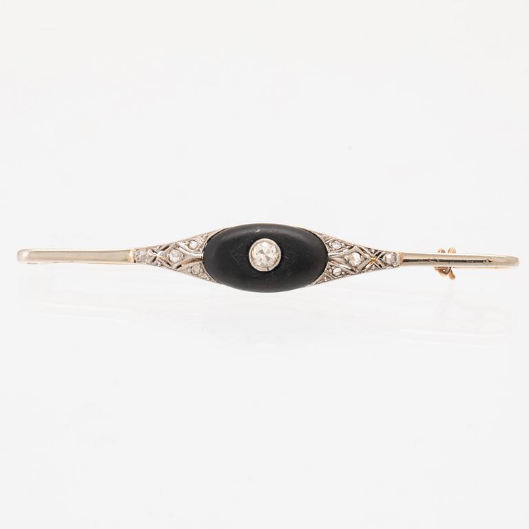 A 14K white and red gold brooch set with round brilliant-cut and rose-cut diamonds and a black stone.