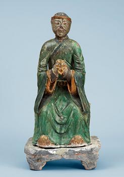 1465. A green and yellow glazed pottery figure of a guardsman, seated on a postament, Ming dynasty.
